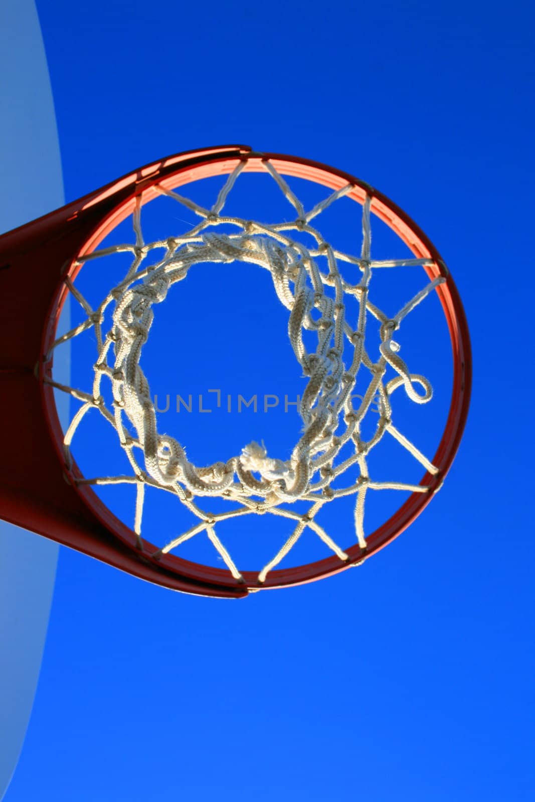 Basketball net and backboard over clear blue sky.
