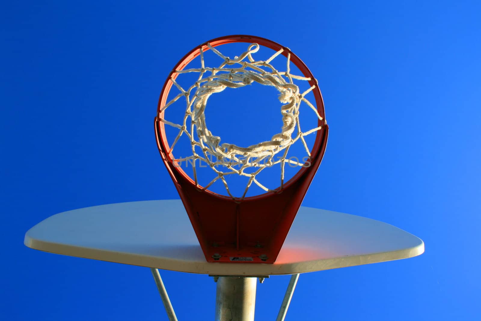 Basketball net and backboard over clear blue sky.
