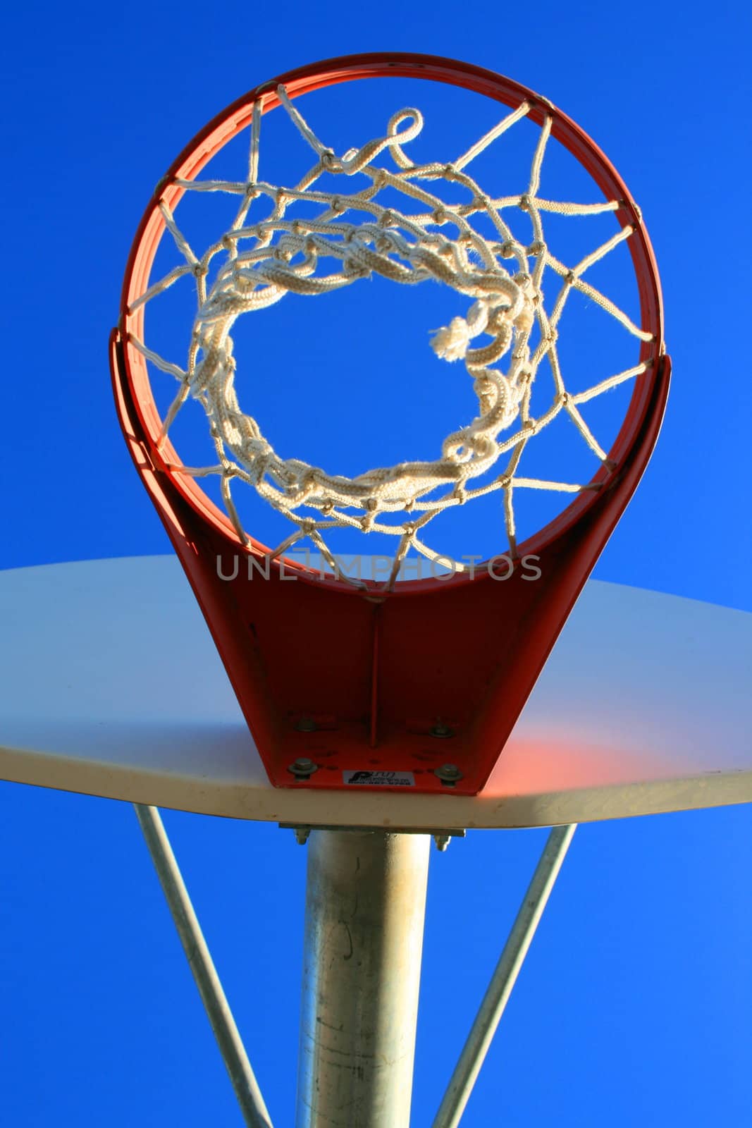 Basketball net and backboard over clear blue sky.
