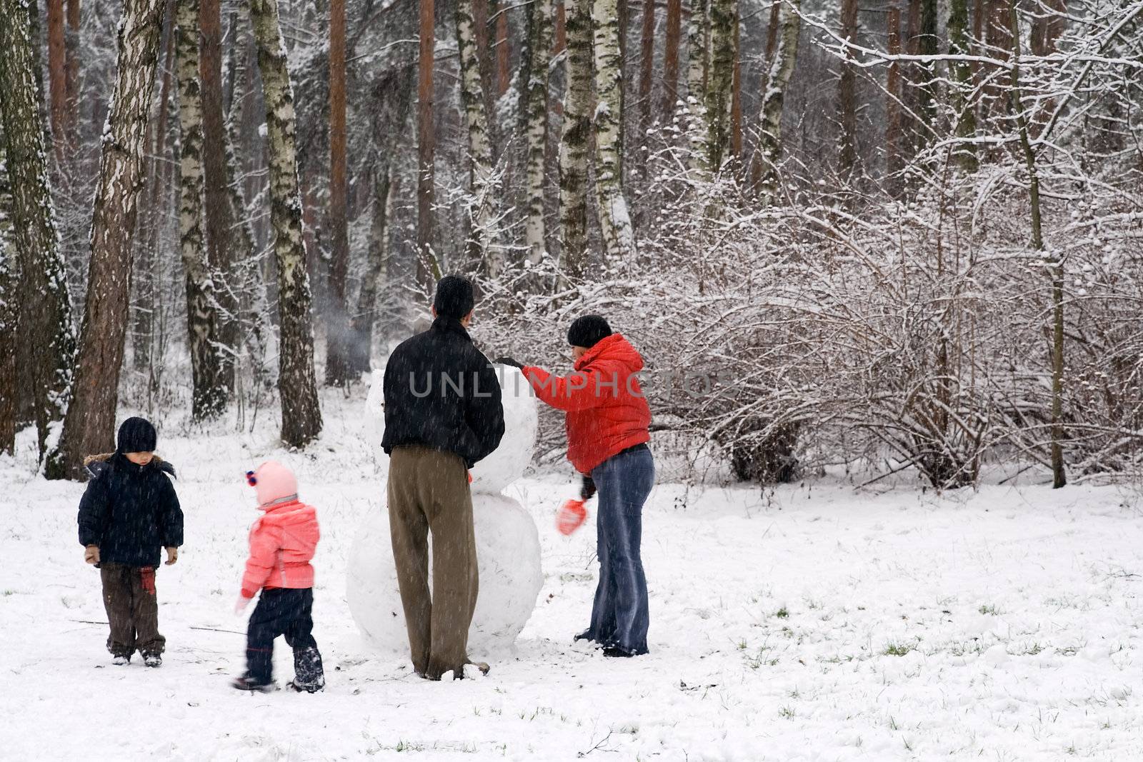 Family Moulding a Snow Man in the Winter Forest