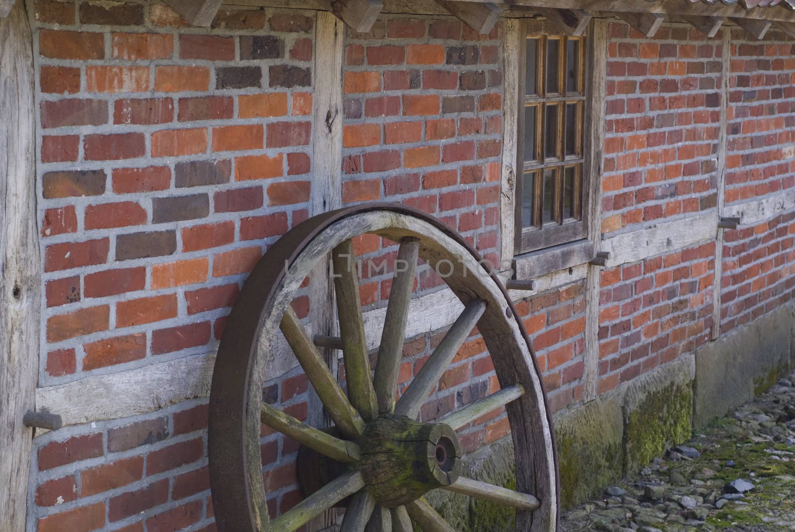 Part of an old wooden wheel in front of an ancient farm.