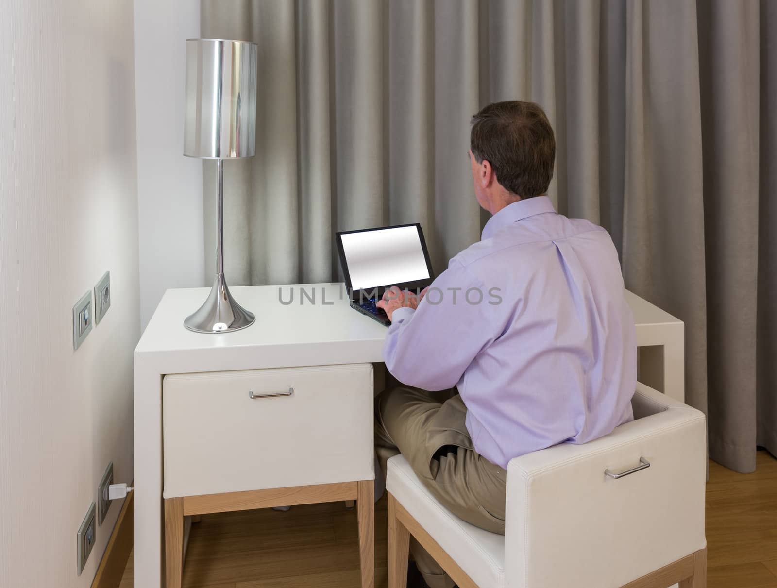 Senior man at modern white table desk and two chairs in hotel room at night