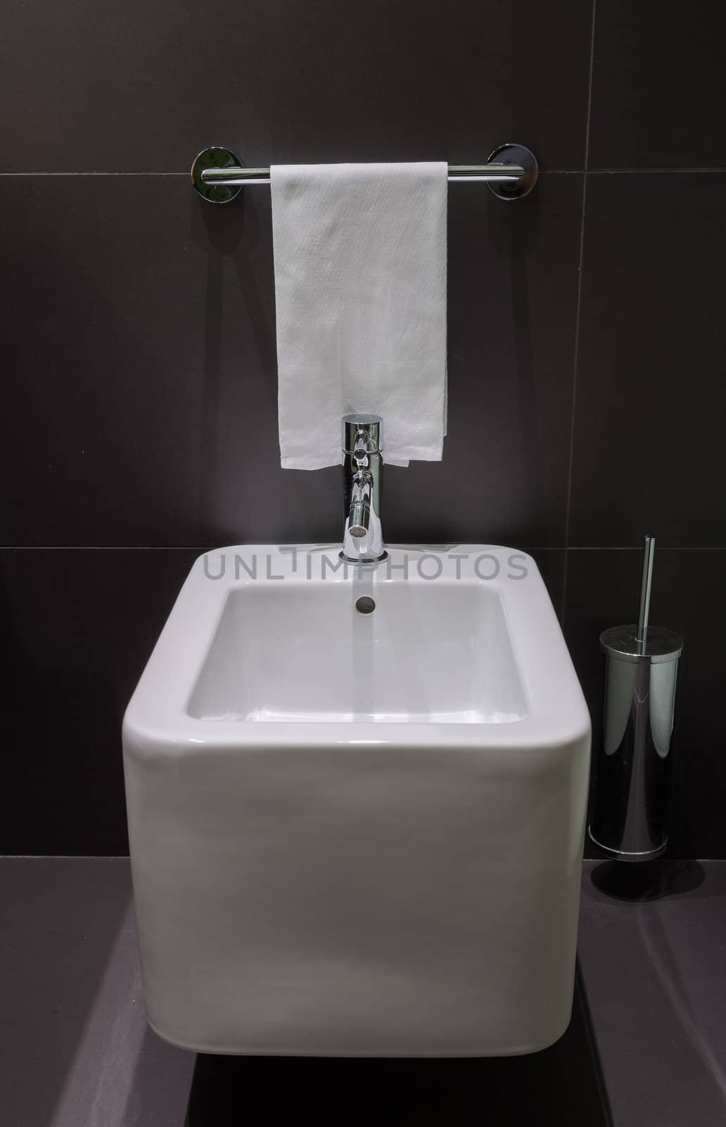 Details of modern square bidet in black tiled bathroom