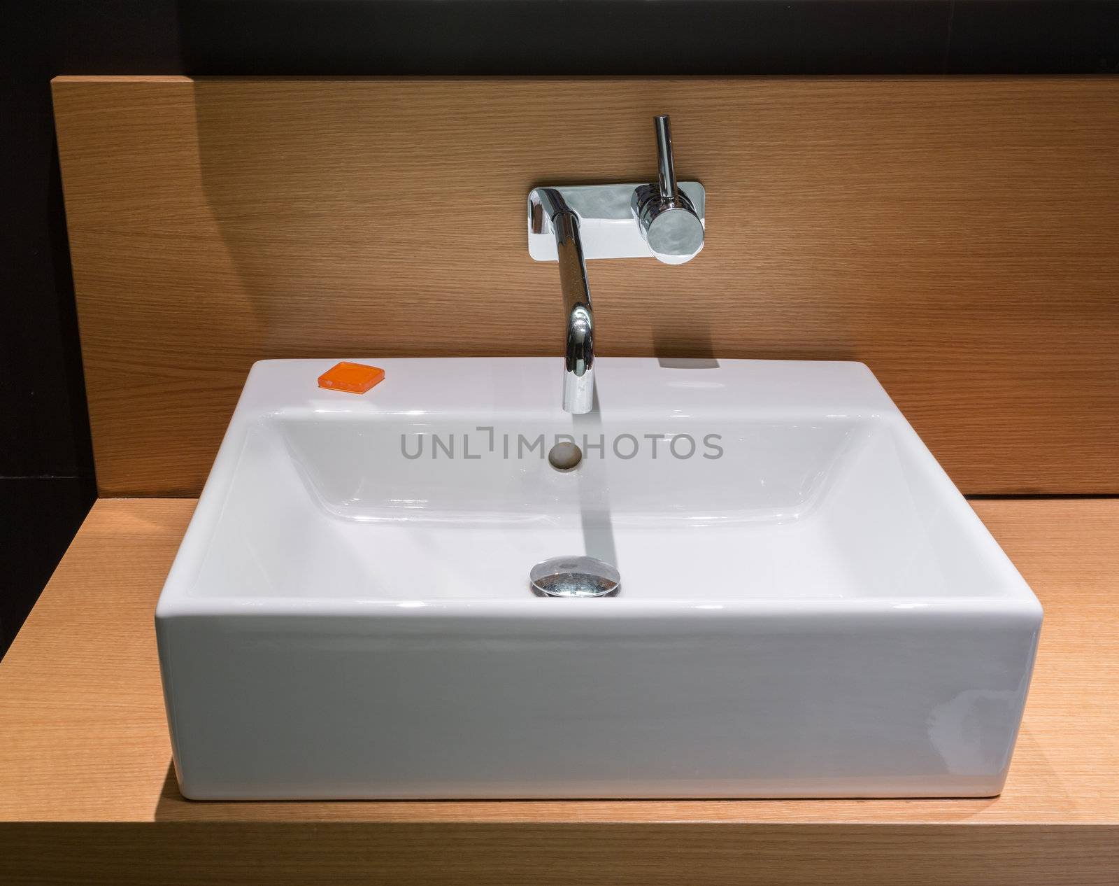 Details of modern square ceramic sink and faucet tap in surface mount on wooden surface
