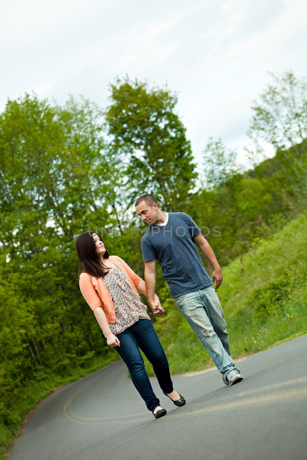 Young happy couple enjoying each others company outdoors walking down an empty road. A very fitting theme for the start of marriage or any romantic relationship.