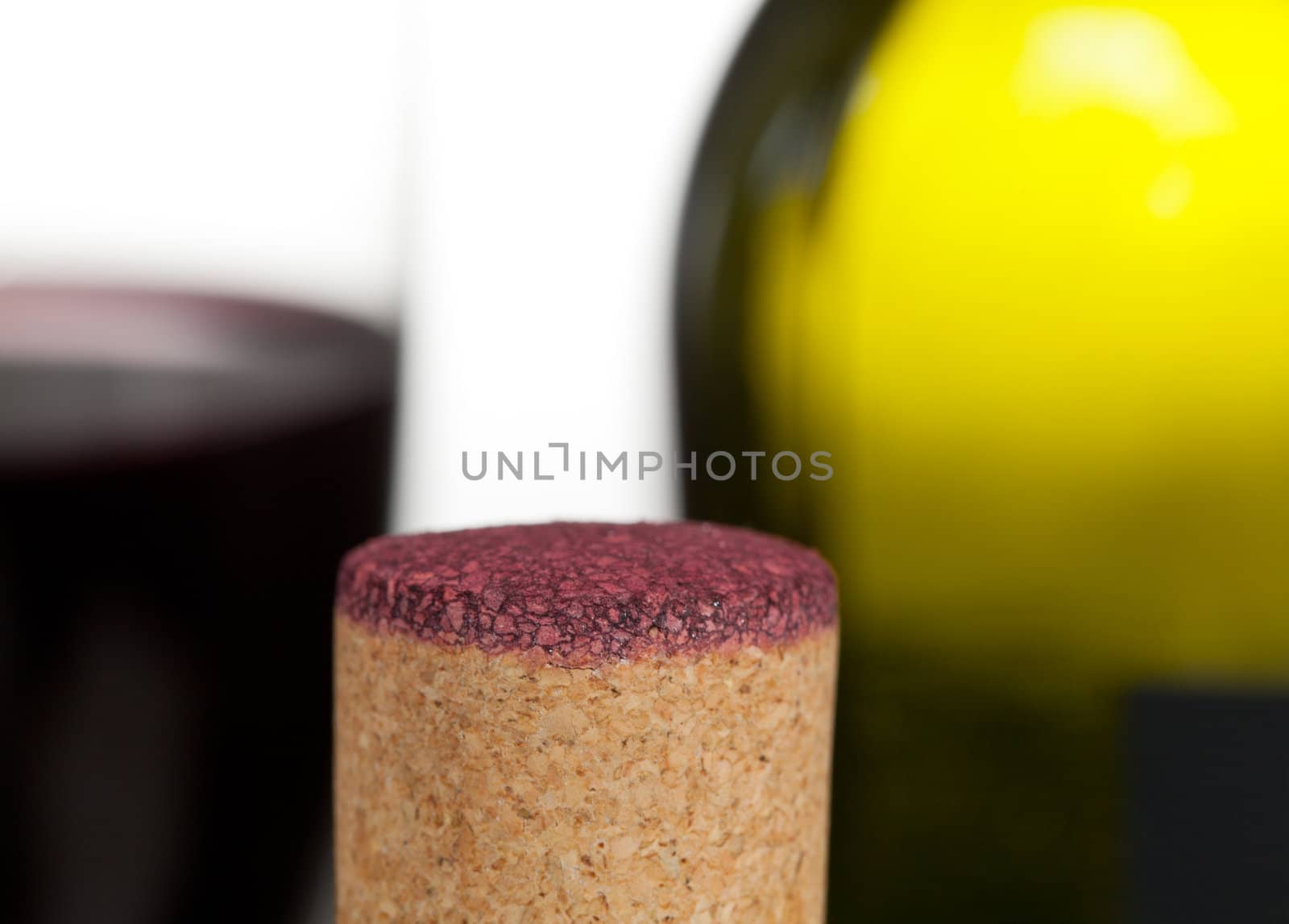 Cork from red wine bottle in front of glass of wine and green bottle out of focus