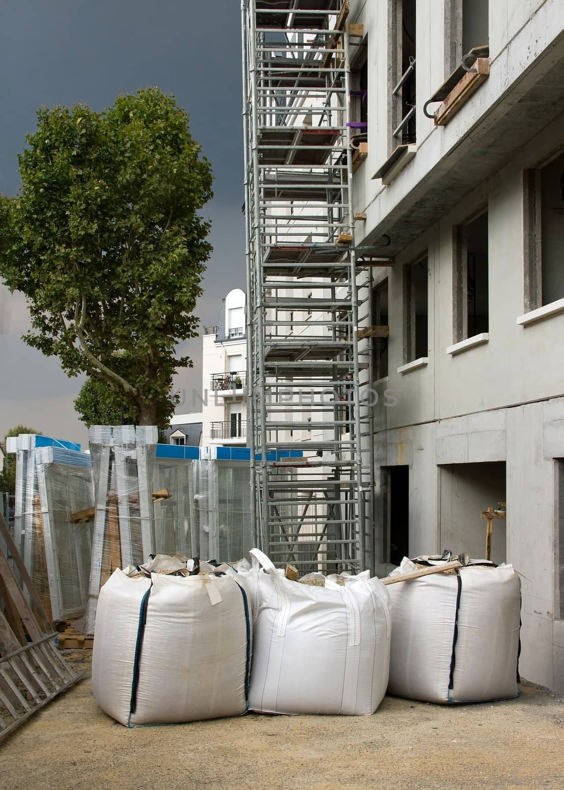 facade of a building under construction, scaffolding and sandbags under a stormy sky