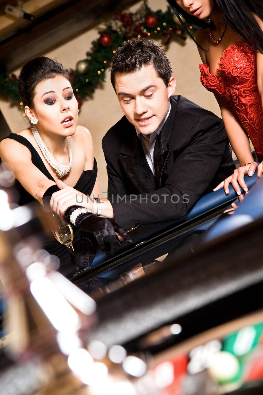 Handsome man and females gamblinng on roulette table in casino