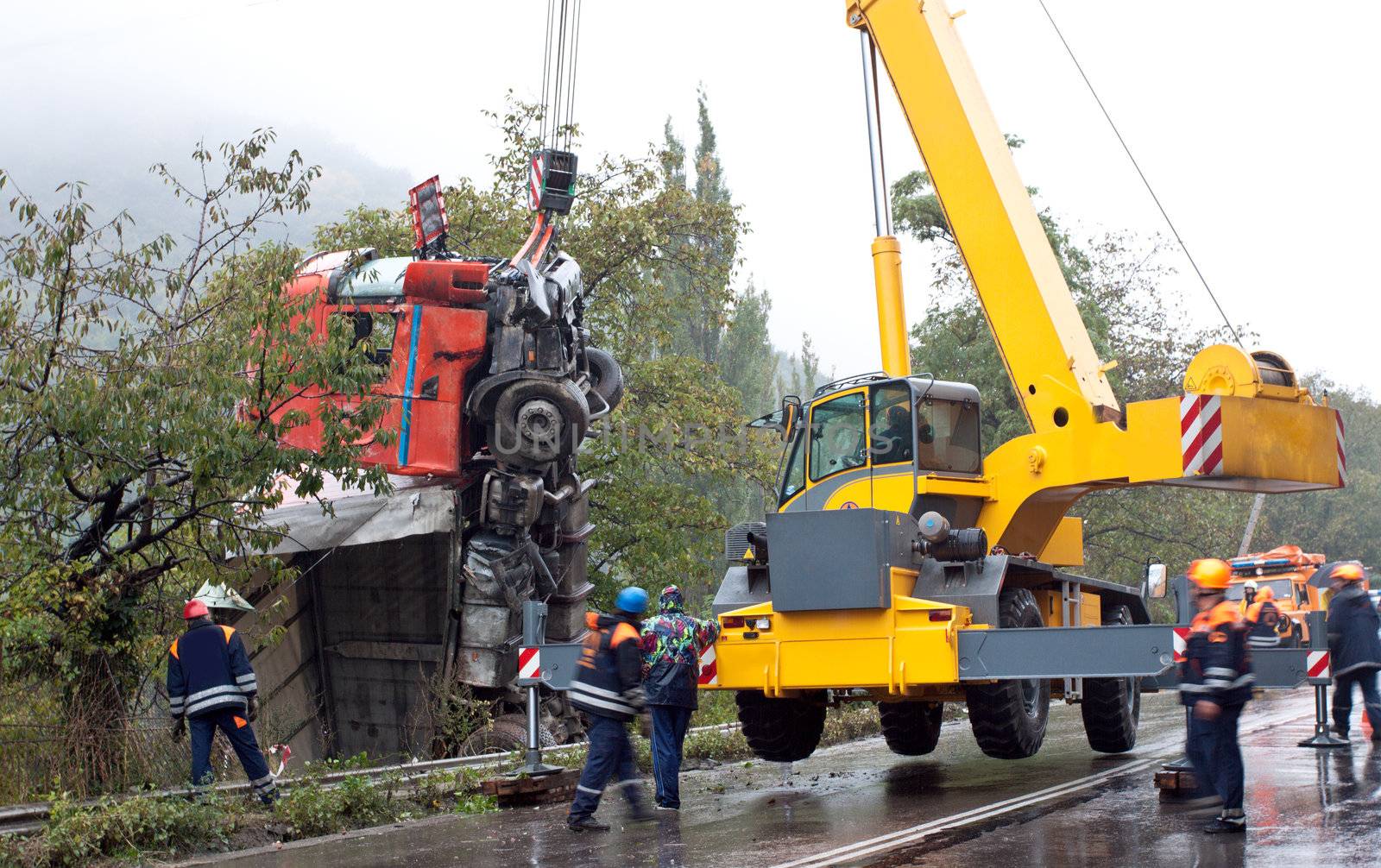 Yellow crane lifting a crashed truck by the road