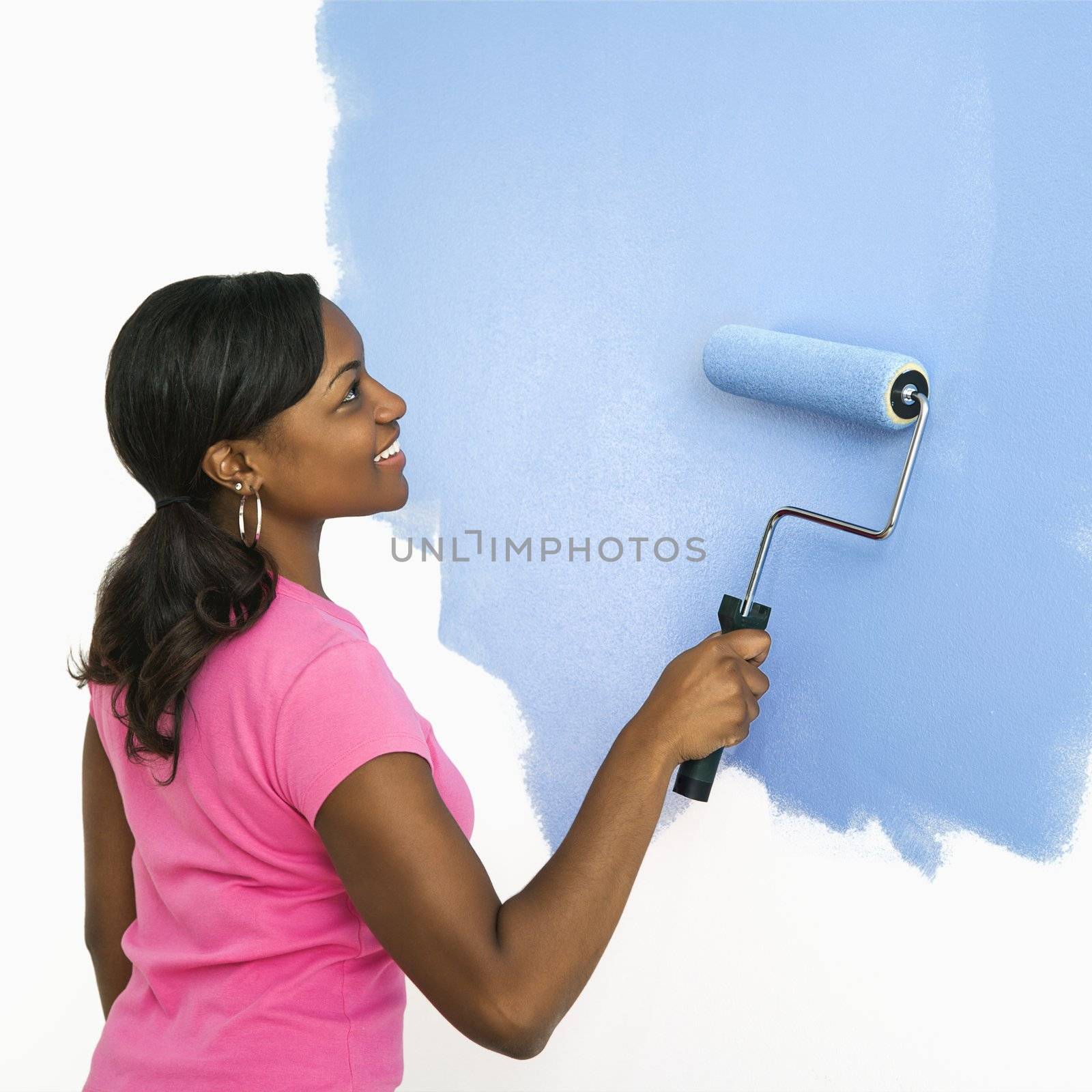 Pretty woman painting wall. by iofoto