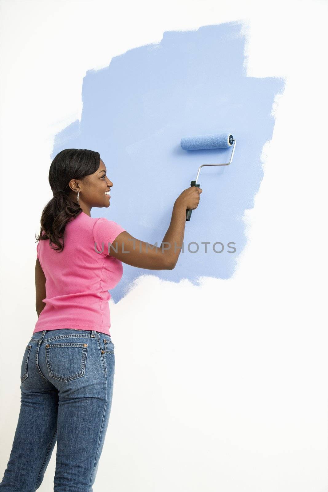 African American woman painting wall blue.