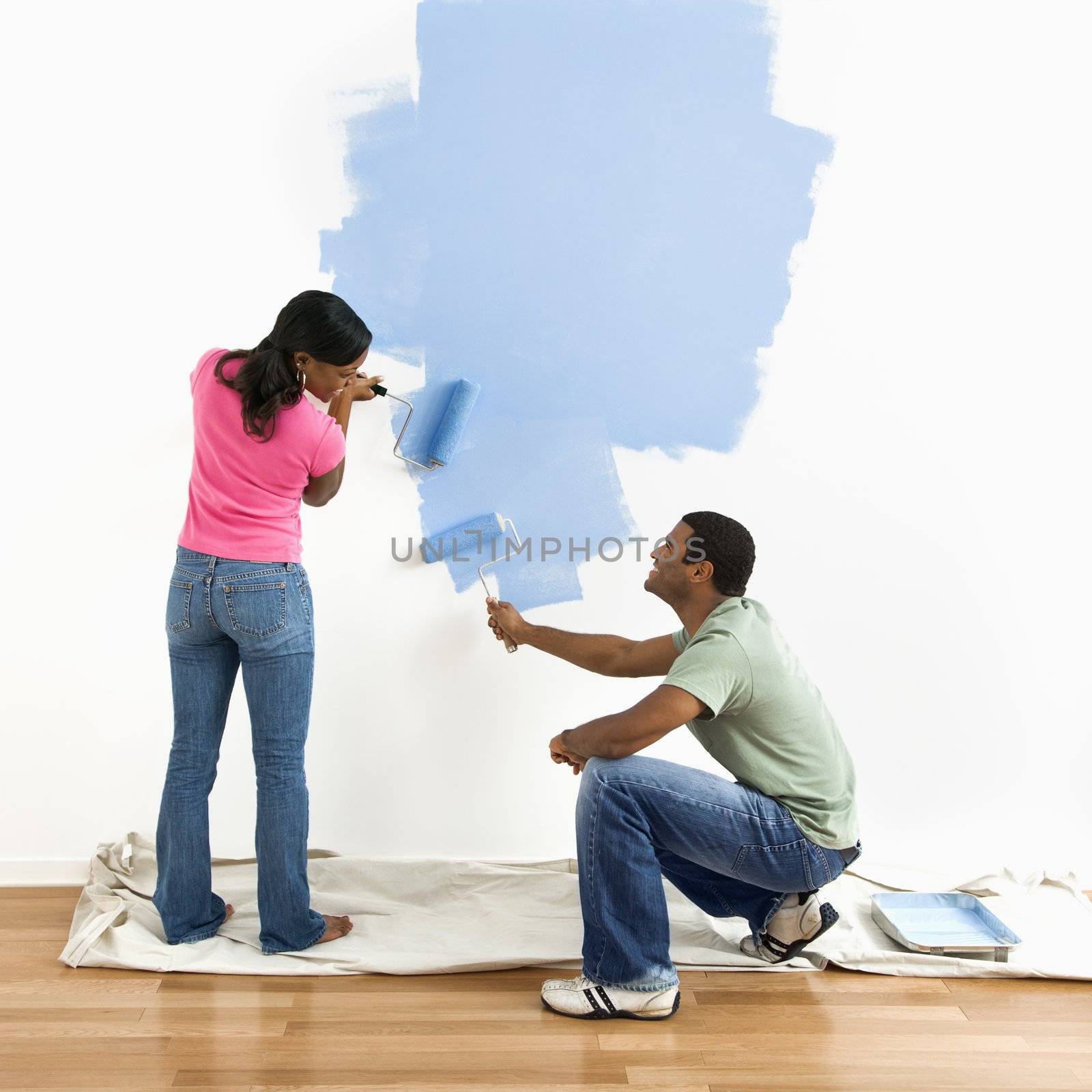 Smiling African American male and female couple painting wall blue.