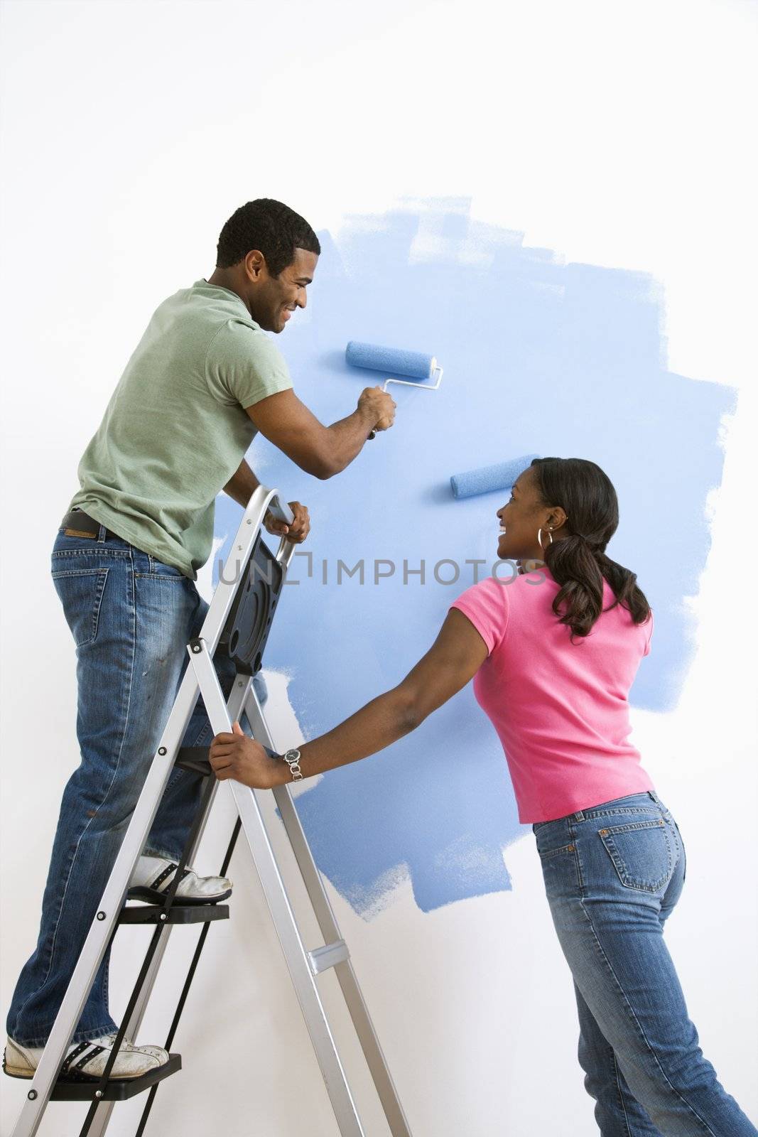 Smiling African American male and female couple painting wall blue.