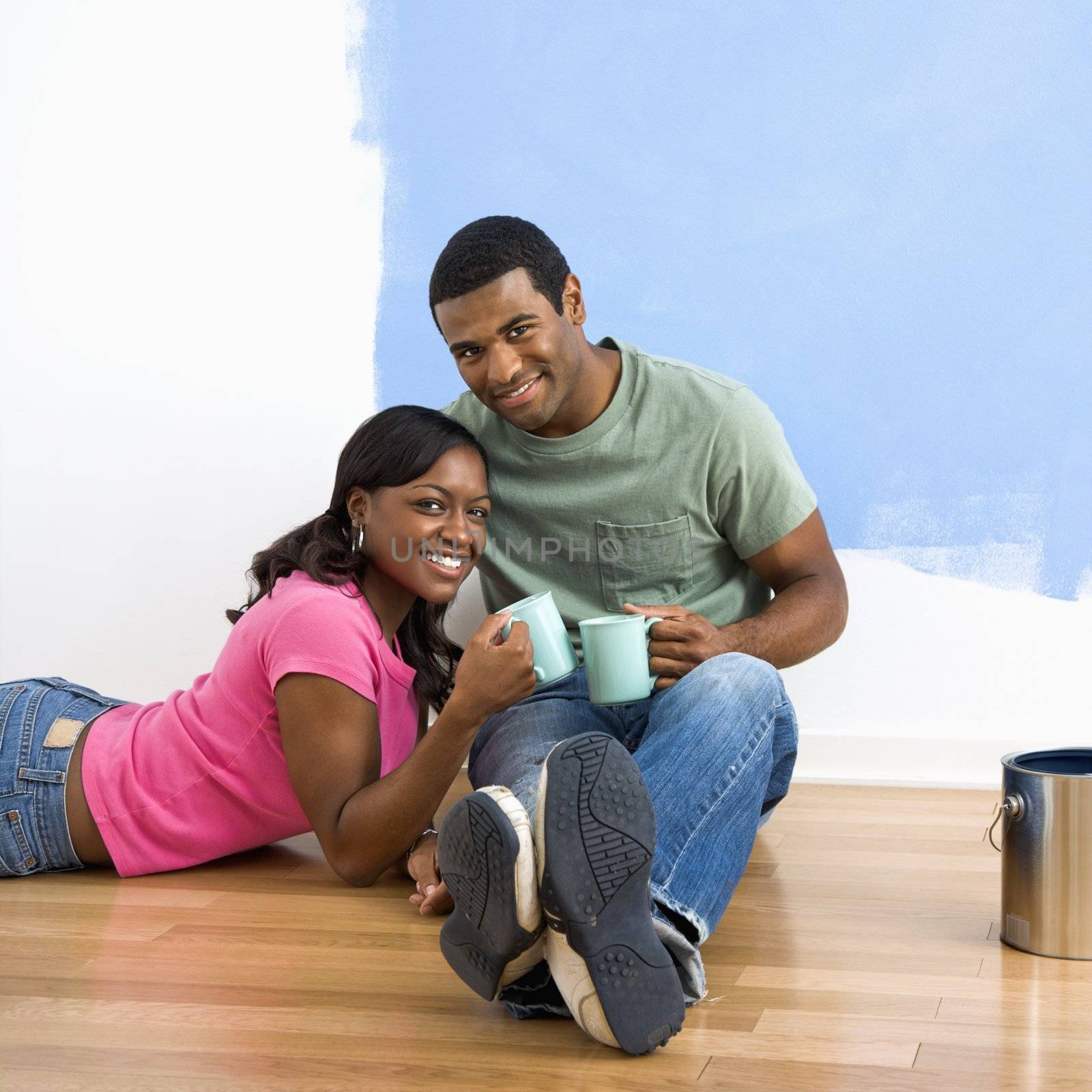 African American couple relaxing together with coffee next to half-painted wall.