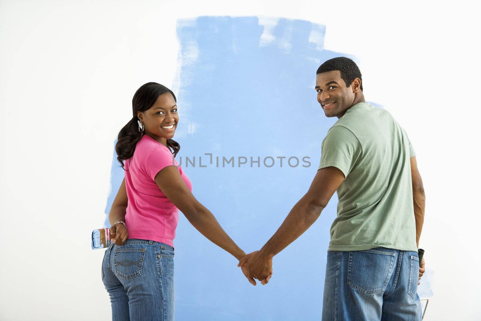 African American couple standing together in front of half-painted wall looking at viewer.