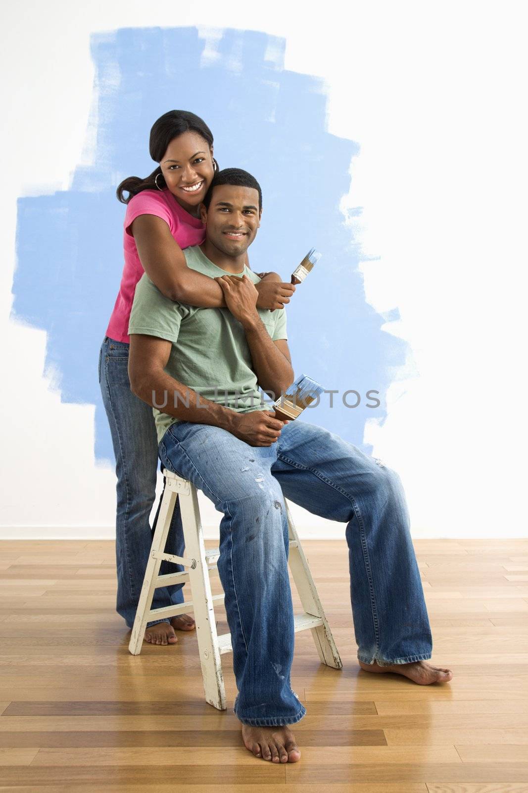 Portrait of African American male and female couple next to half-painted wall.