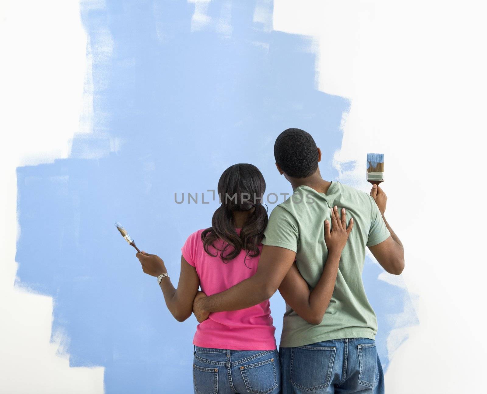 African American couple standing together looking at half-painted wall.