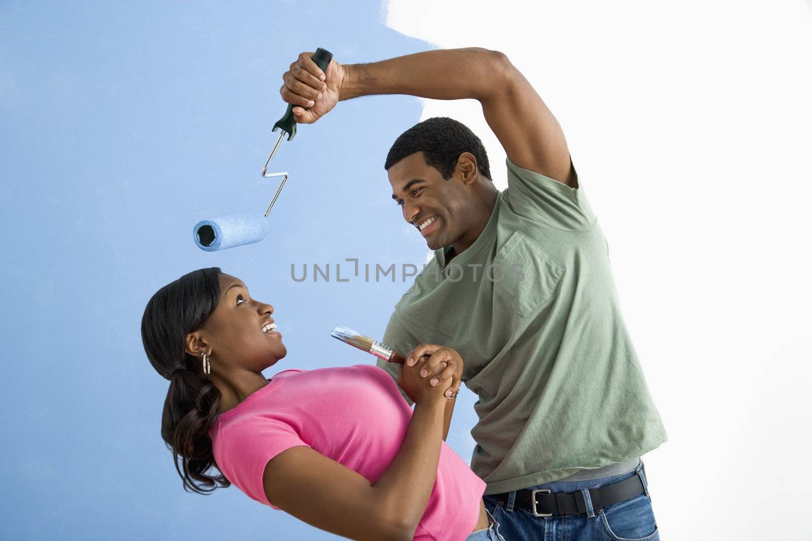 African American young man pretending to paint woman's face with paint roller.