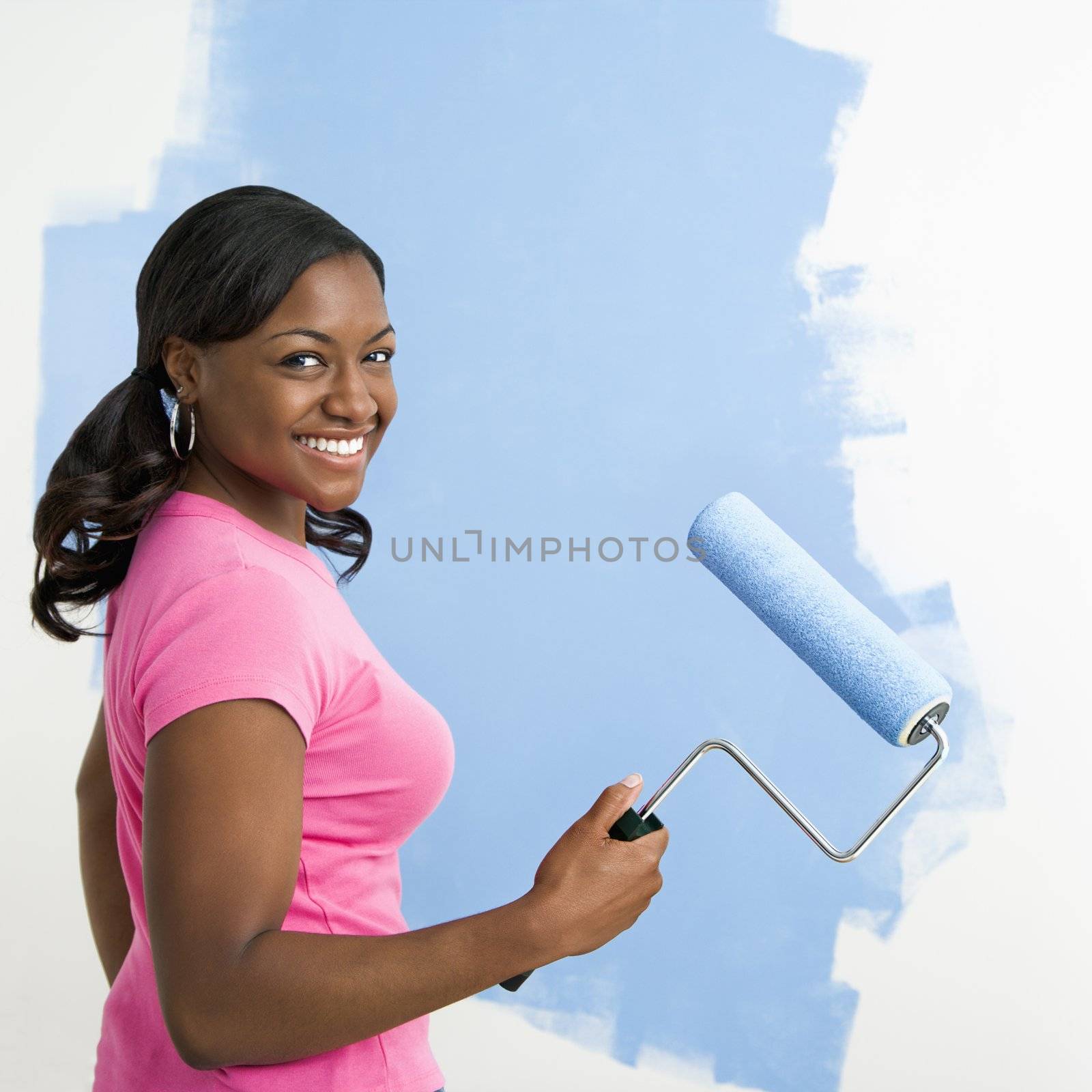 African American woman painting wall blue smiling at viewer.