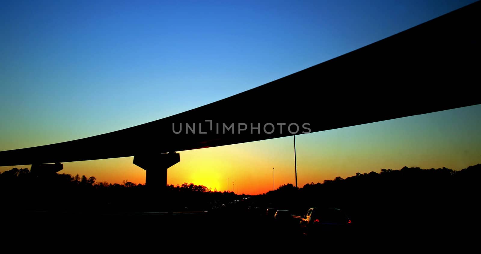 Silhouette of a bridge from a road at sunset.