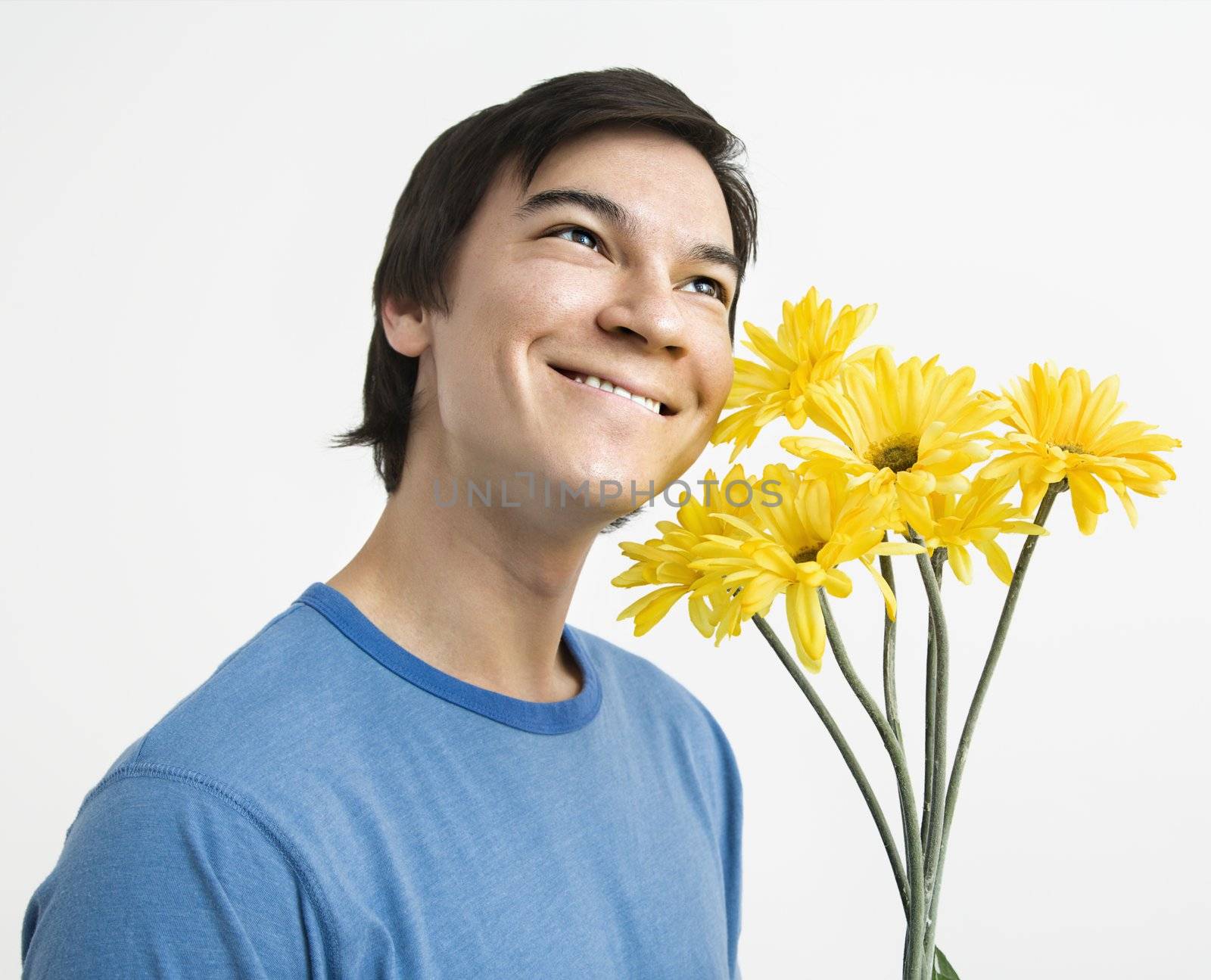 Asian young man holding bouquet of yellow gerber daisies smiling.