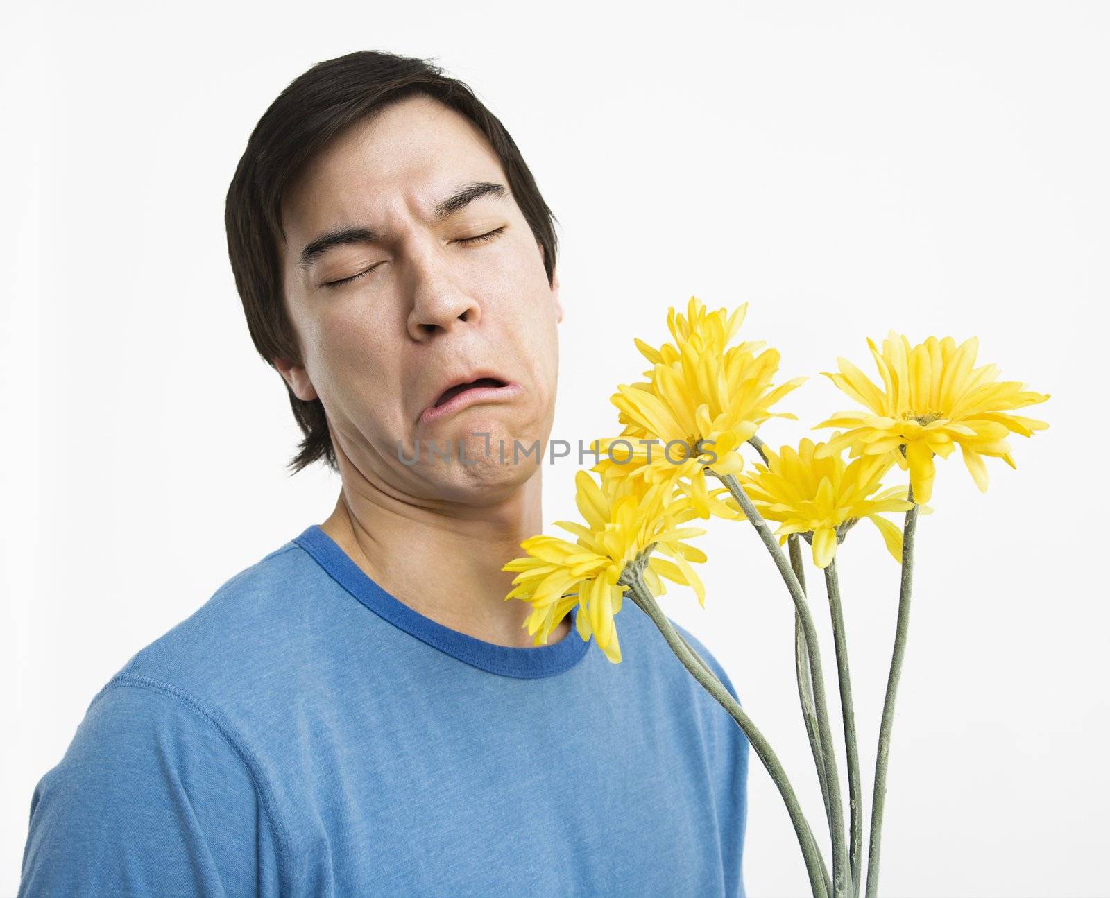 Asian young man holding bouquet of yellow gerber daisies with bad look on his face.