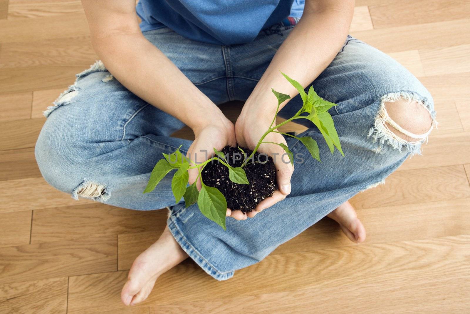 Man sitting on floor holding growing cayenne plant.