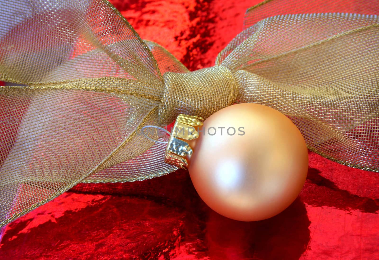 A gold Christmas ornament and gold bow on a red metallic background.