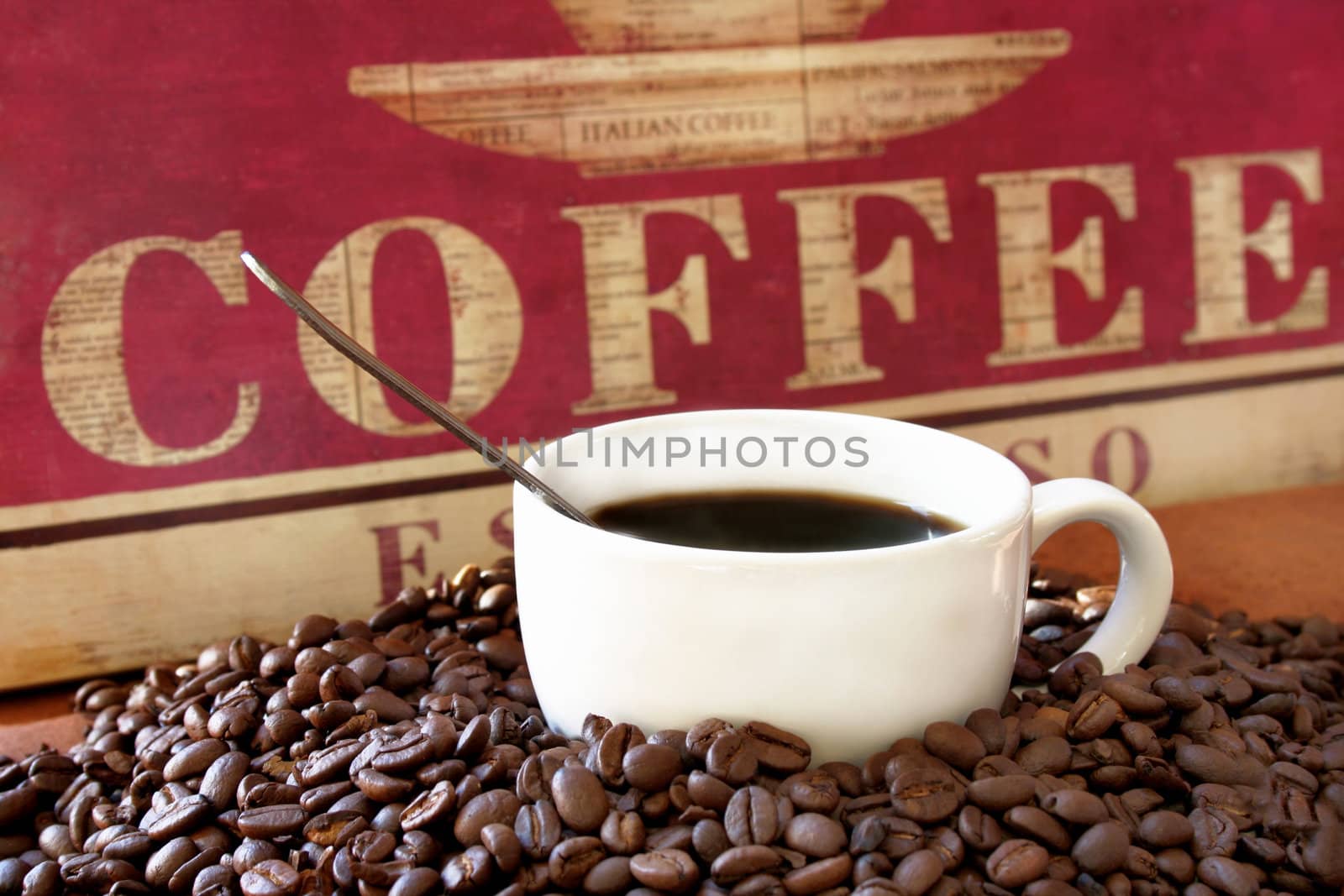 Cup of coffee surrounded by coffee beans and a handmade sign with the word coffee in the background.