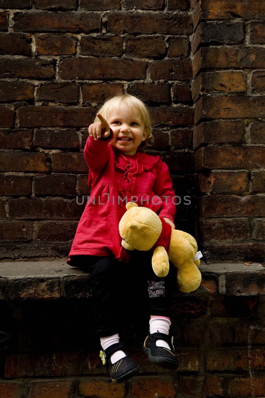 blonde little girl is sitting with teddy bear and laughing