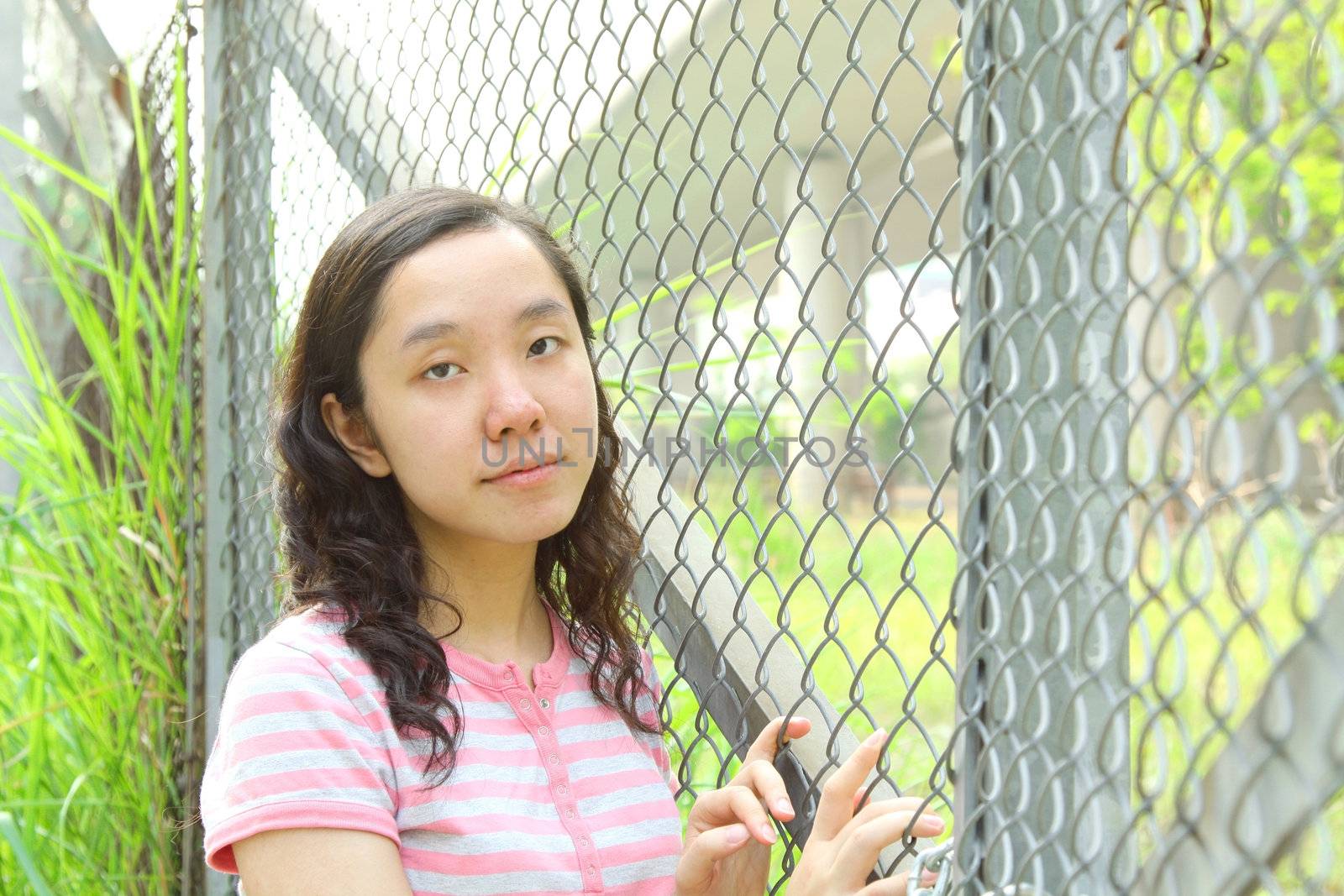 Asian girl with sad face, standing next to a net. She wants to escape from now's life. 