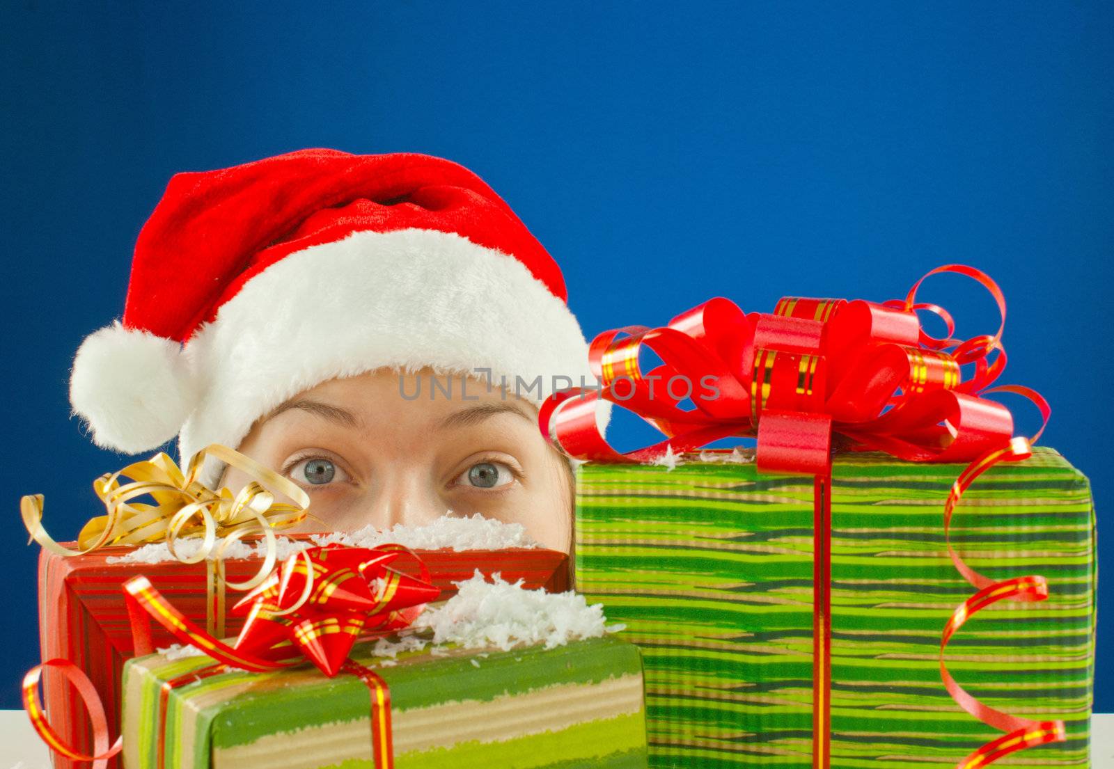 Surprised teen girl looking from behind the Christmas presents