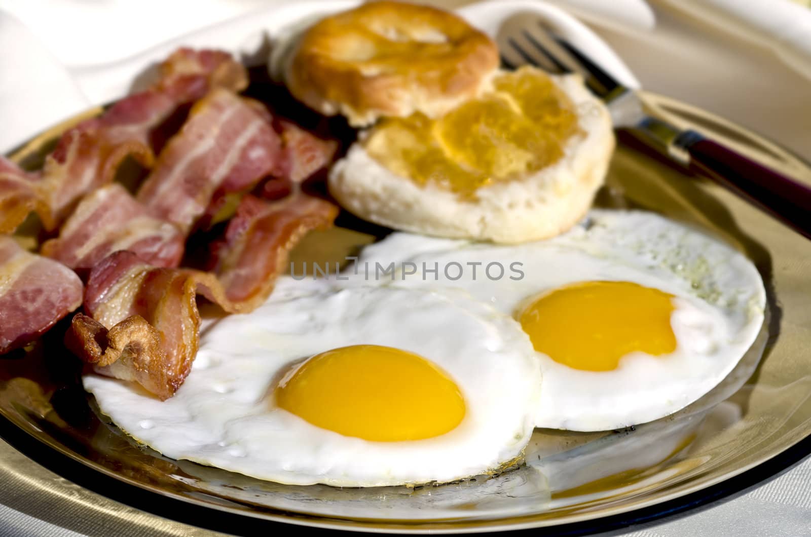 Breakfast plate outside with eggs, bacon, and biscuits with apple jelly.