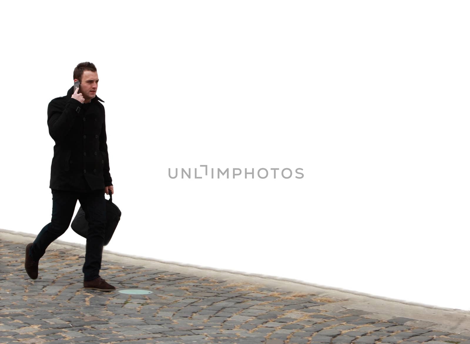 Businessman walking on a cobbled street in front of a white wall while using his mobile.