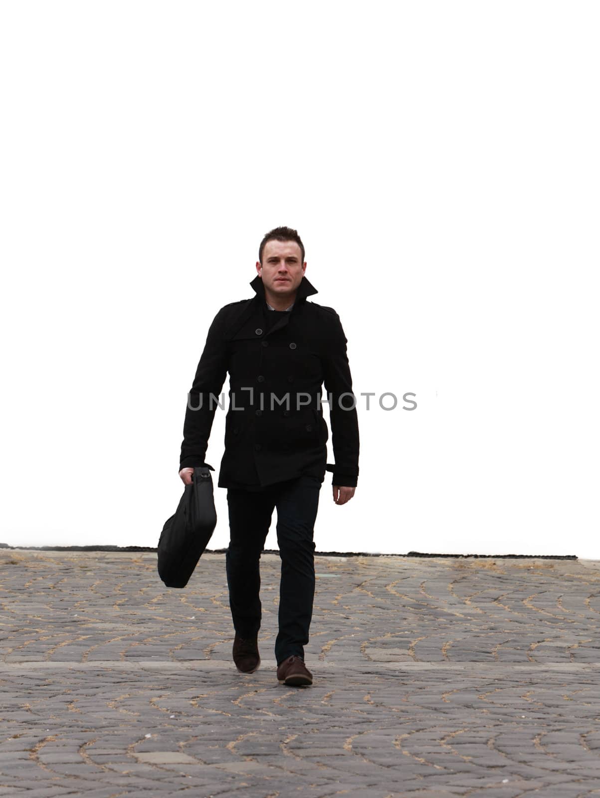 Young businessman walking through the camera on a cobbled street in front of a white wall.