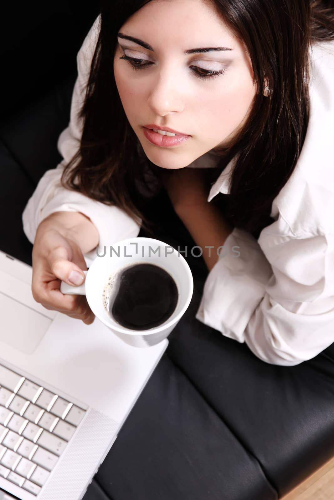 A young, hispanic adult girl watching a Laptop while drinking coffee.