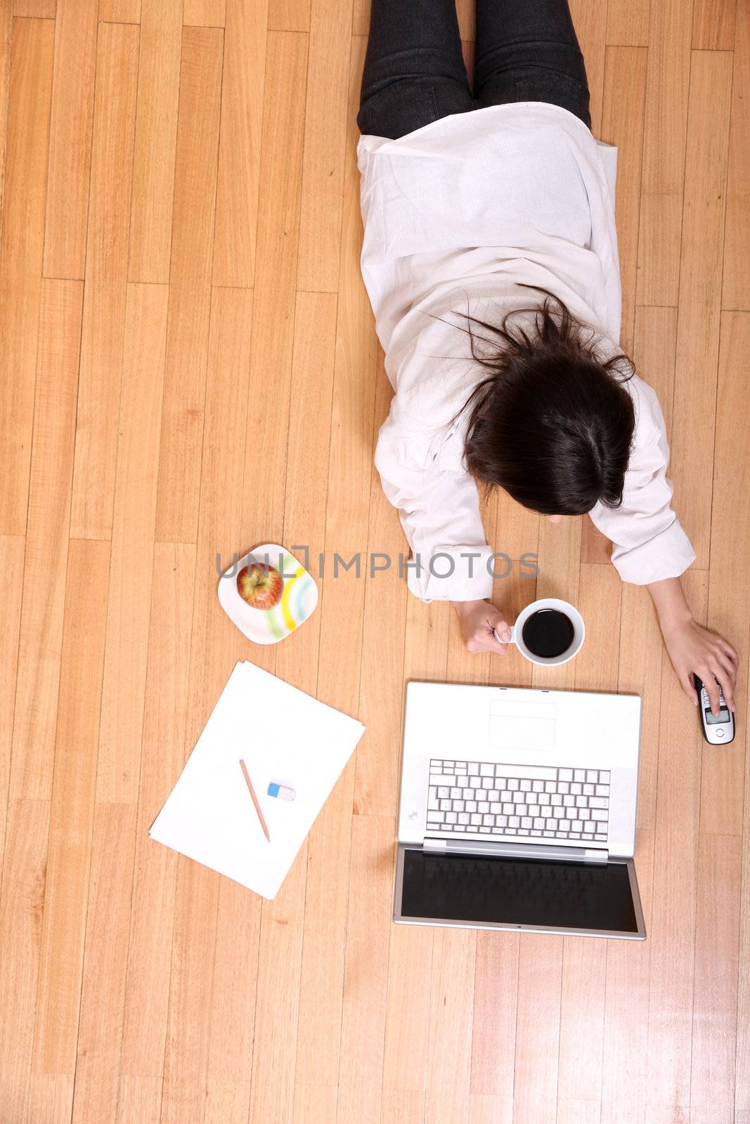 A young adult woman studying on the floor.
