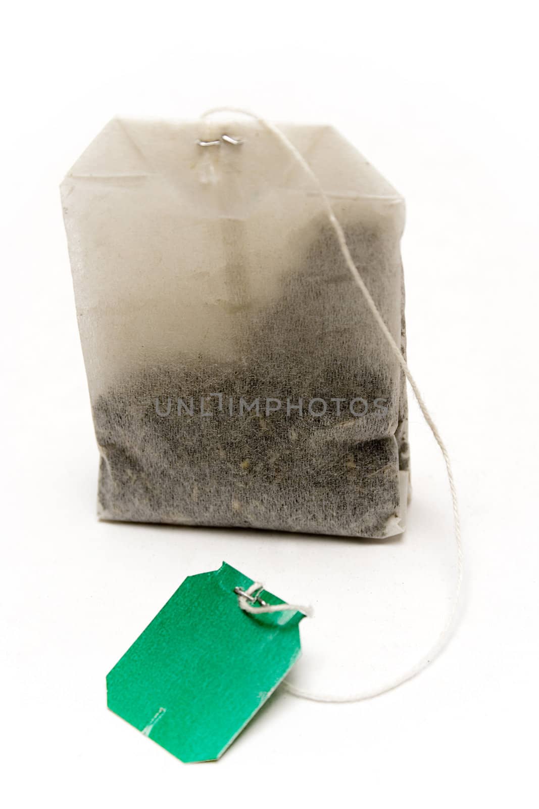 Dry teabag with green tag isolated on a white background.