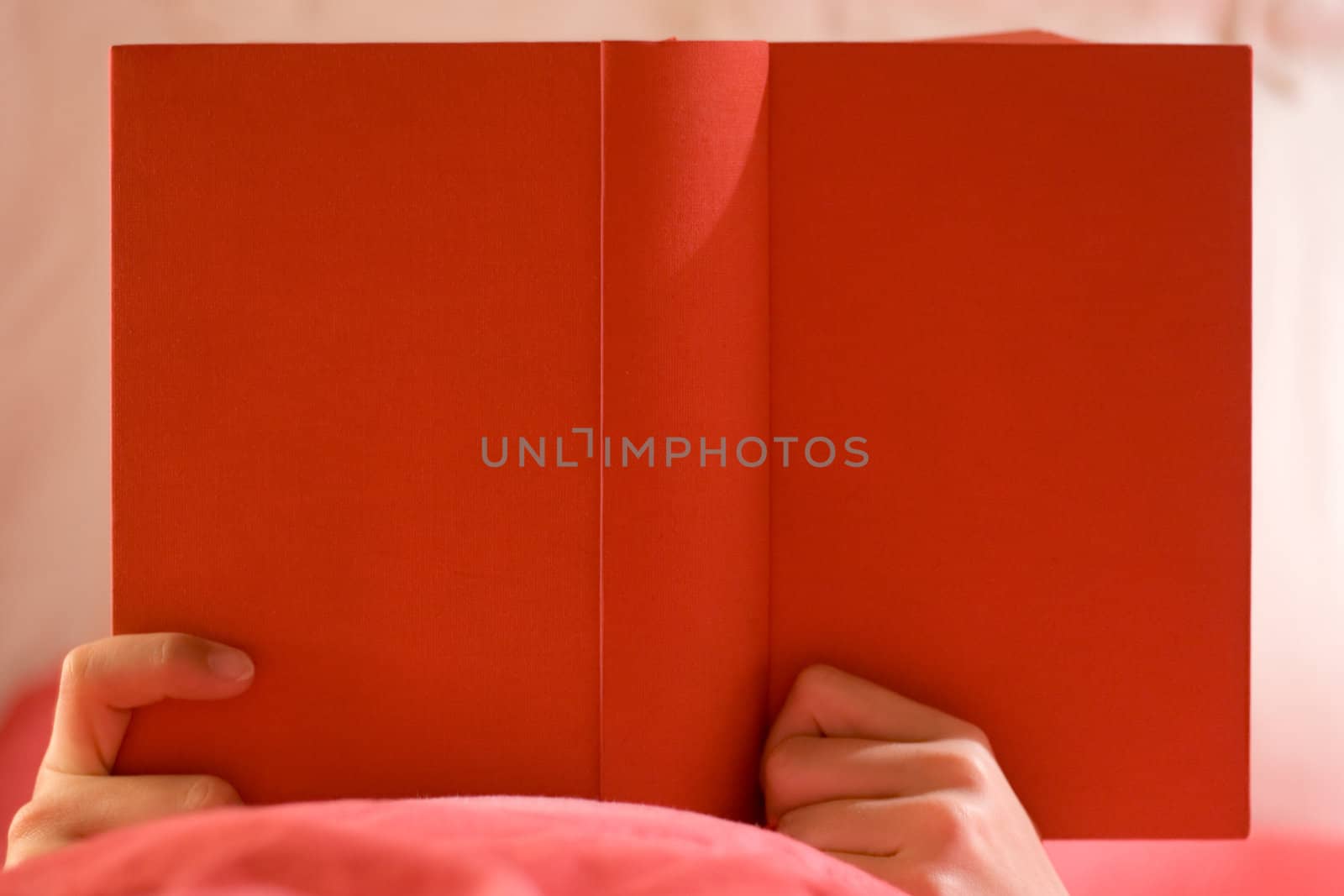 Person in bed reading in a red book.