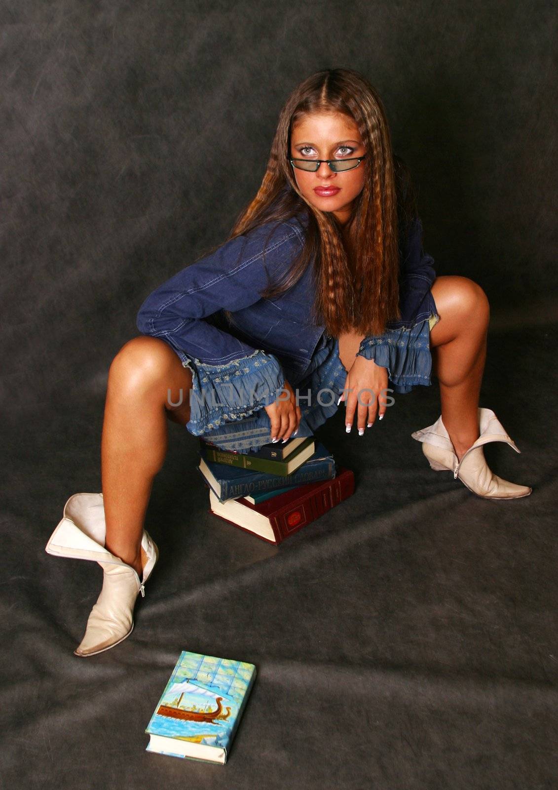 The beautiful girl in glasses sits on books