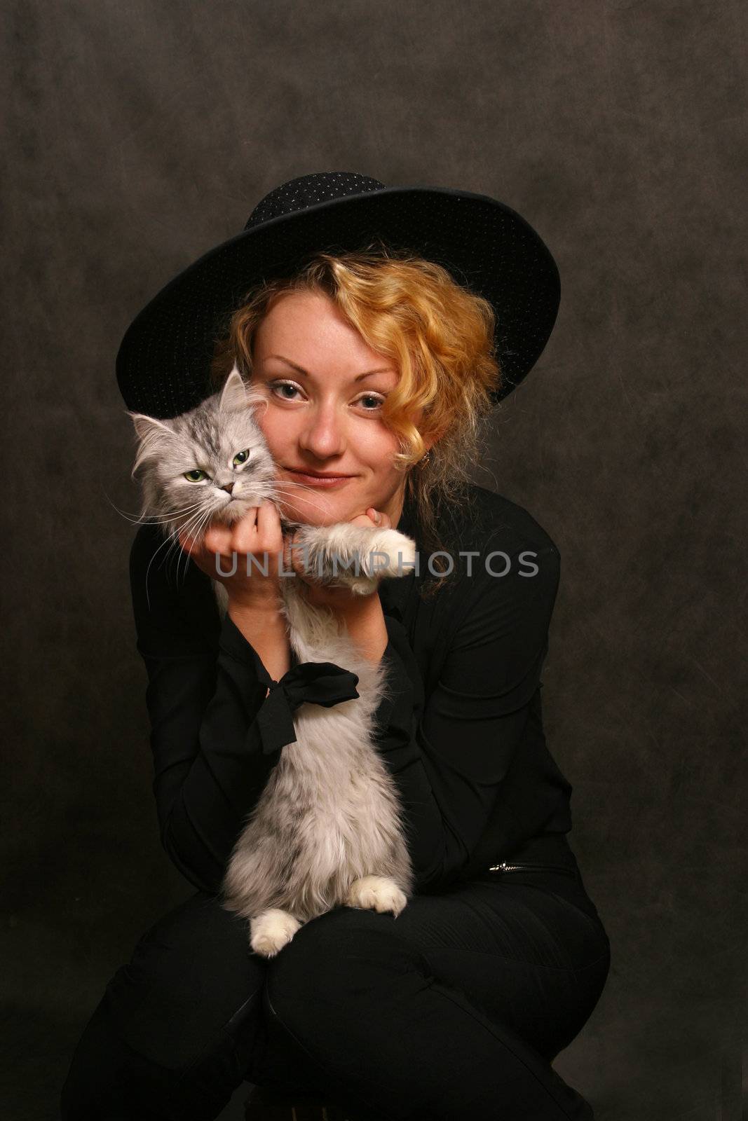 The beautiful girl in a black hat covers a kitten