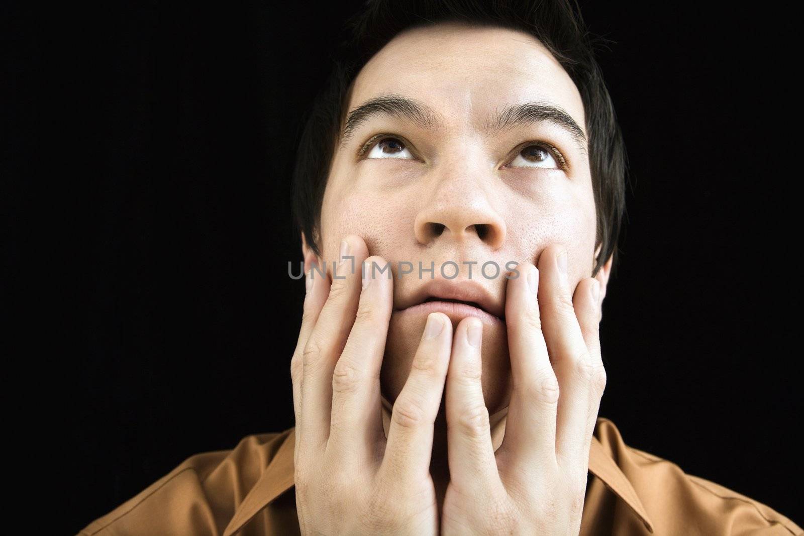 Portrait of Asian young man with hands on face looking up.