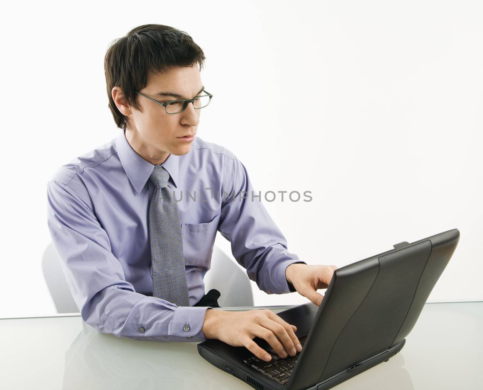 Asian businessman sitting at desk working on laptop computer.