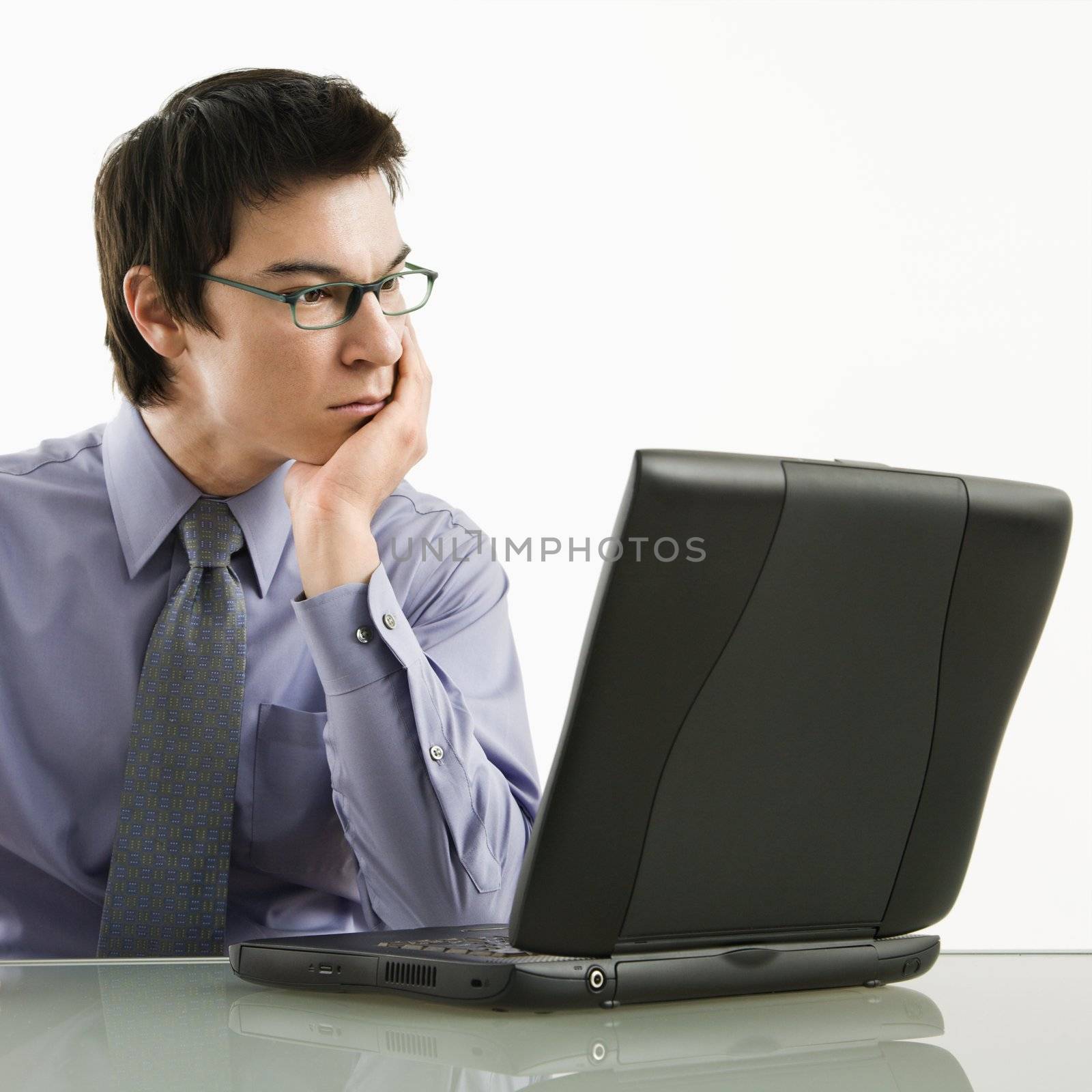 Asian businessman sitting at desk working on laptop computer.