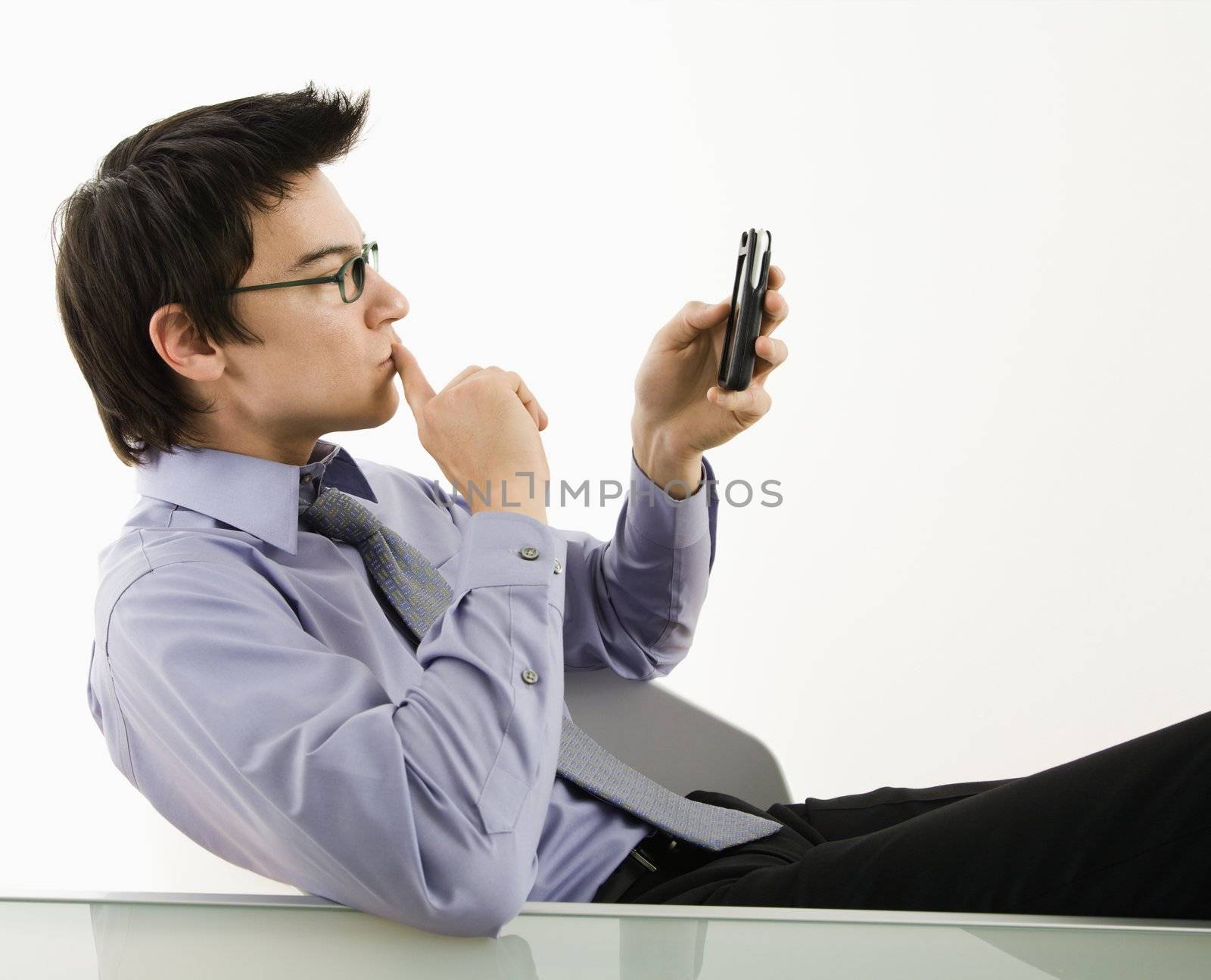 Asian businessman sitting at desk texting using his pda cellphone.