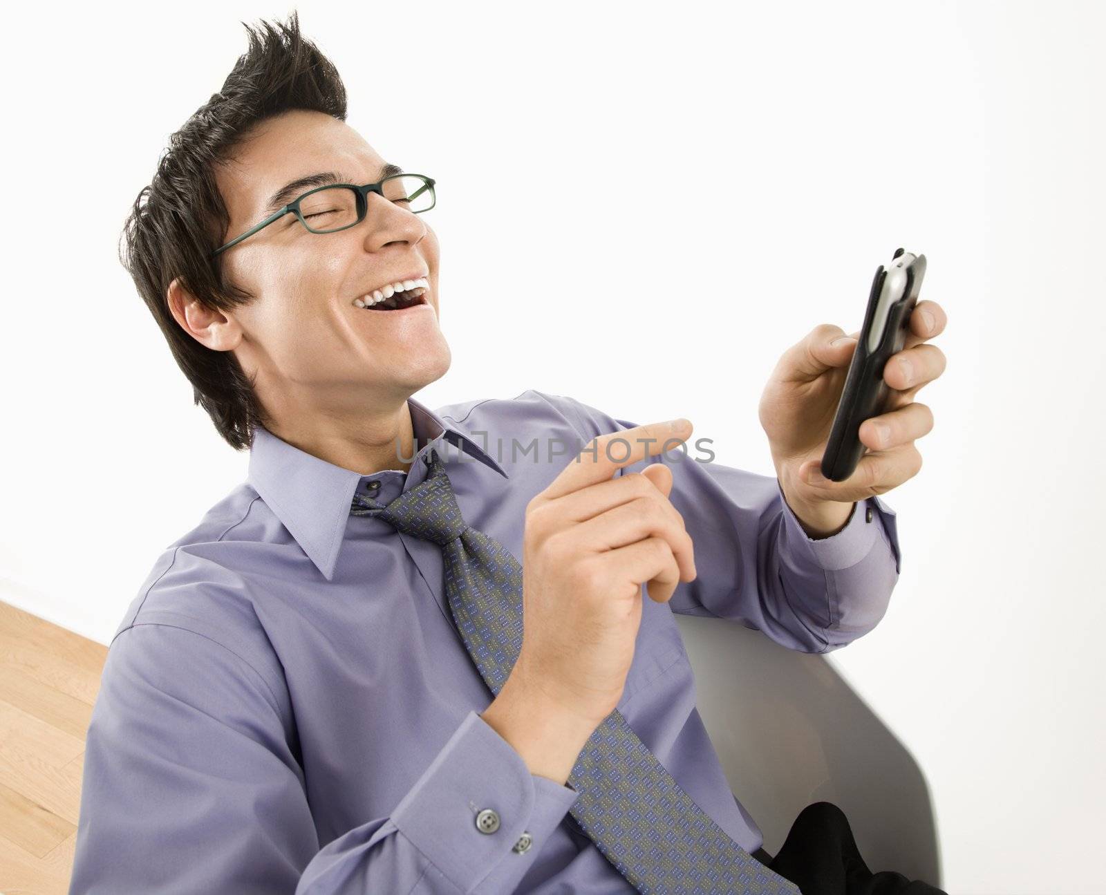 Laughing Asian businessman sitting at desk texting using his pda cellphone.