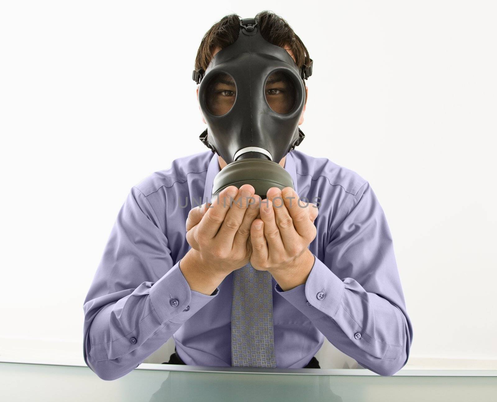 Businessman sitting wearing gas mask holding his hands over his mouth.