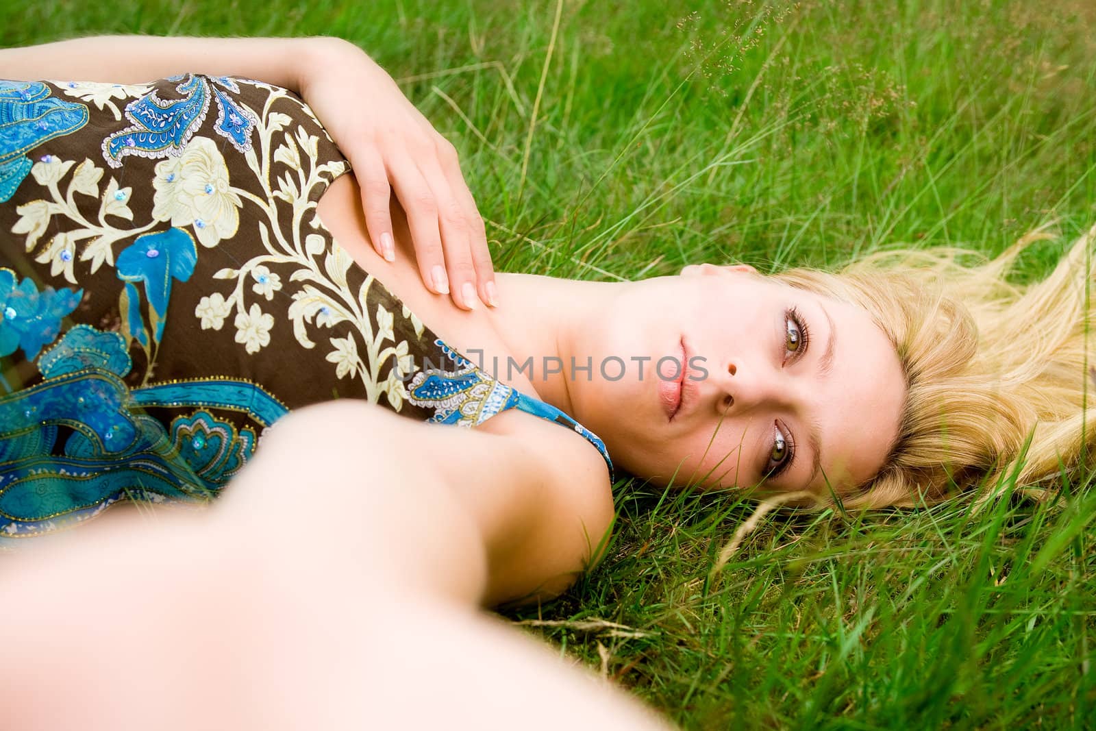 Young beautiful blond girl laying down on the green grass