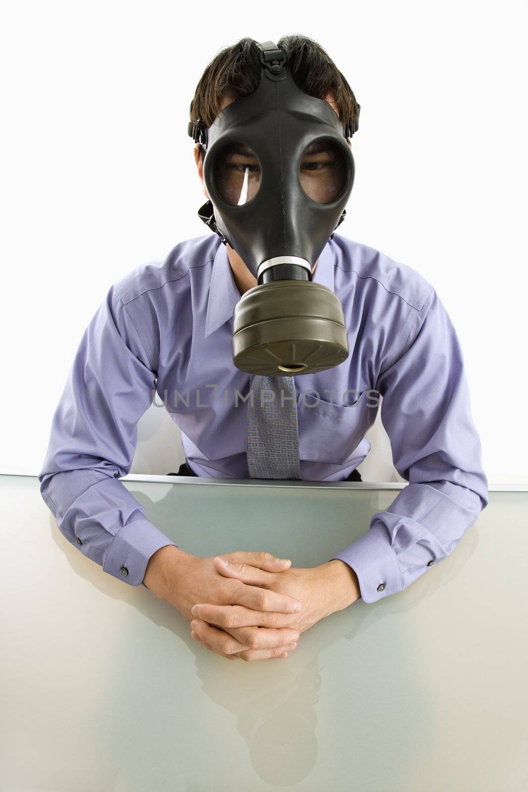 Businessman sitting in white room wearing gas mask.