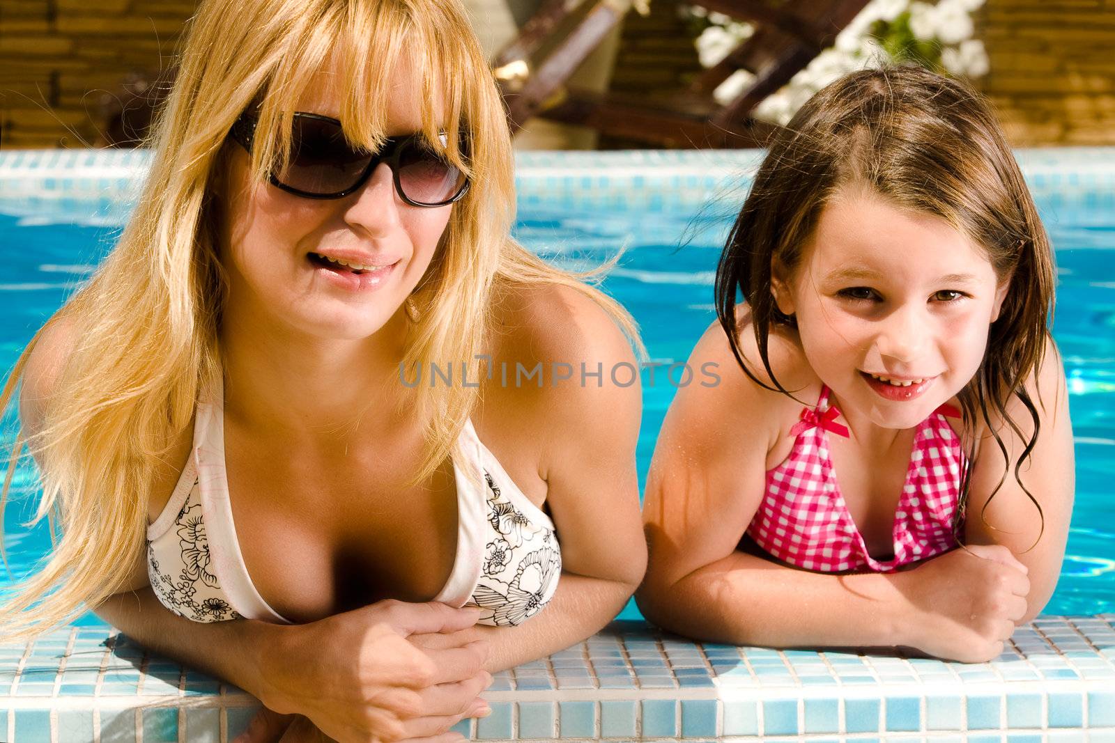 Young blond girl and her sister enjoying the sun in and around the swimming pool
